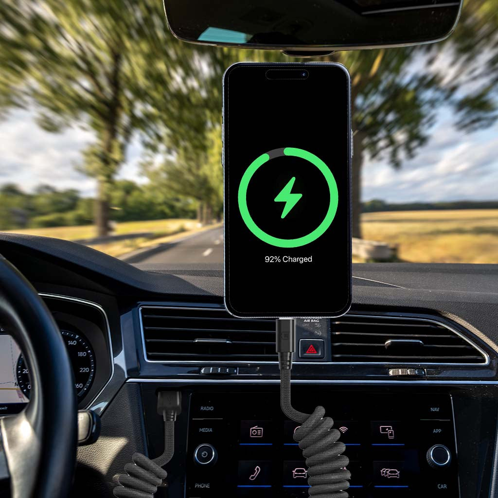 Car dashboard with phone mounted on holder, charging with black coiled USB-C to Lightning cable, 92% battery charge displayed on phone screen