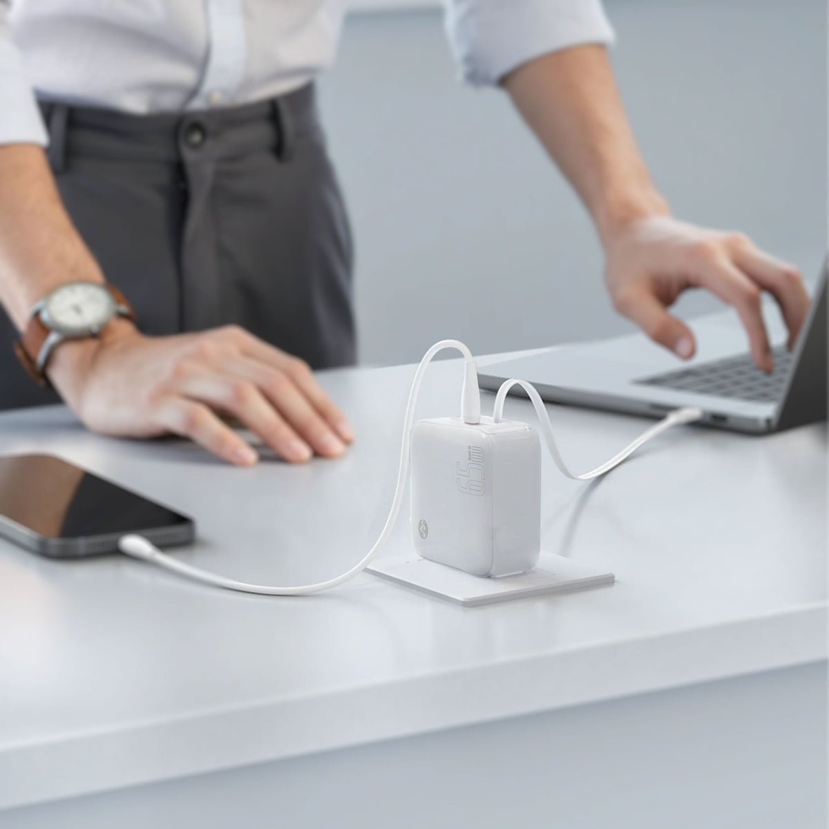 Person plugging the white foldable wall charger into a wall socket, with a laptop nearby, demonstrating portable charging solution
